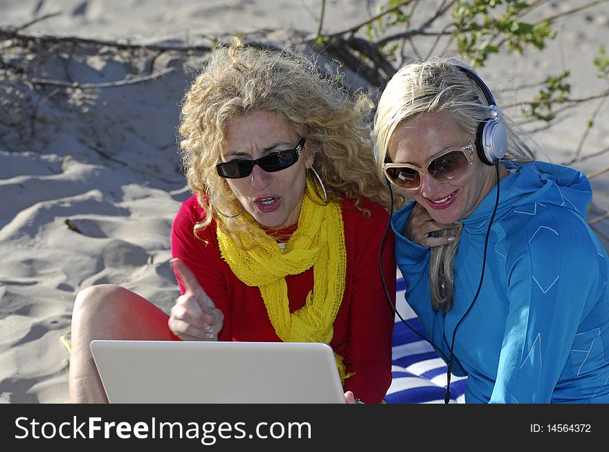 Two beautiful business women work on their laptop and enjoy some beach time. Two beautiful business women work on their laptop and enjoy some beach time.