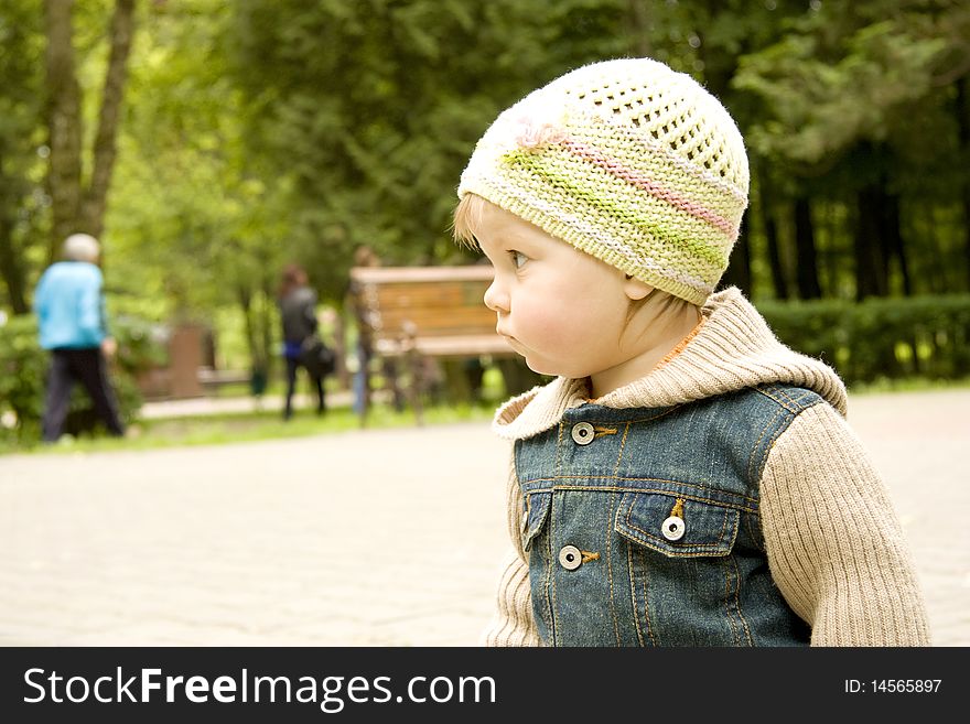 The child in park dressed in a cap and a jacket looks aside. The child in park dressed in a cap and a jacket looks aside