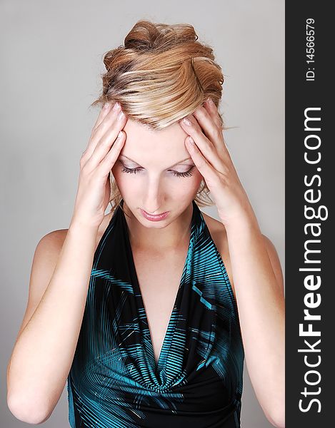 A beautiful blond woman holding her hands on her head to rap of her hurting head, on light gray background. A beautiful blond woman holding her hands on her head to rap of her hurting head, on light gray background.