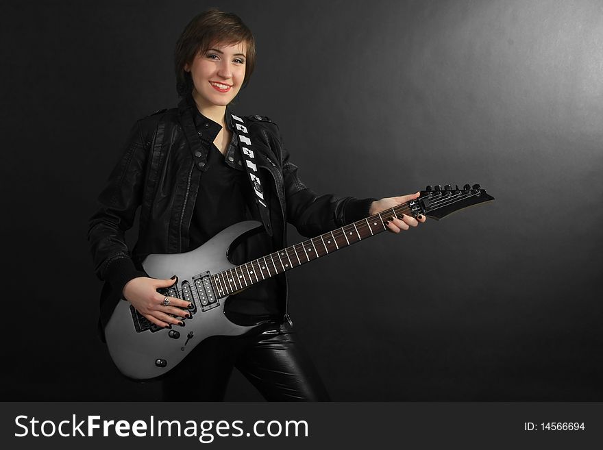 Rock girl in leather outfit with electric guitar on black background