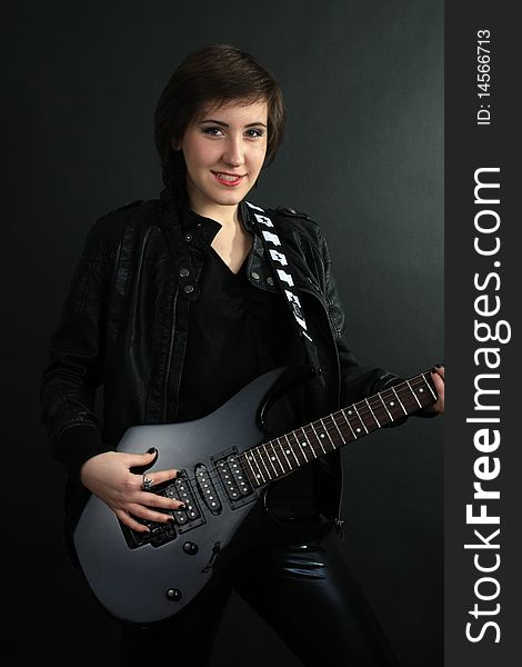 Rock girl in leather outfit with electric guitar on black background