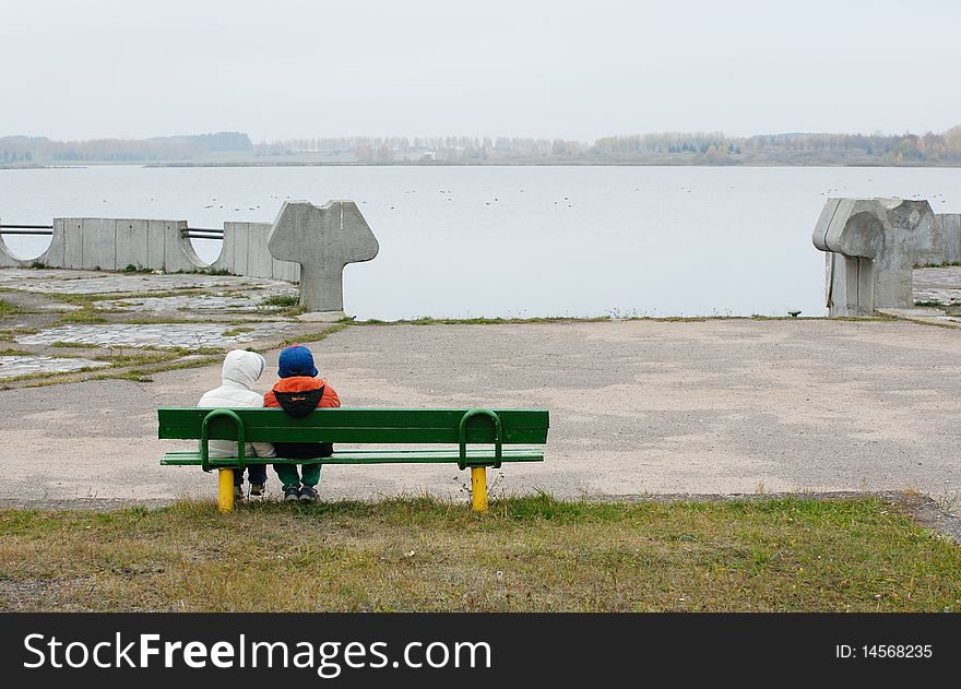 Overcast autumn day, children on a bench on the lake. Overcast autumn day, children on a bench on the lake