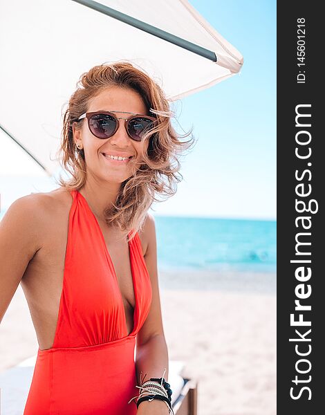 Young Woman In Swimsuit With Cocktail Glass On White Beach Sitting On Sunbed