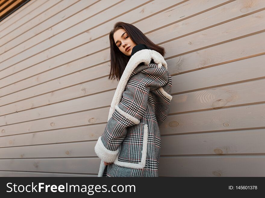 Young pretty attractive woman in a luxurious checkered jacket  with white fur in retro style is posing on the street