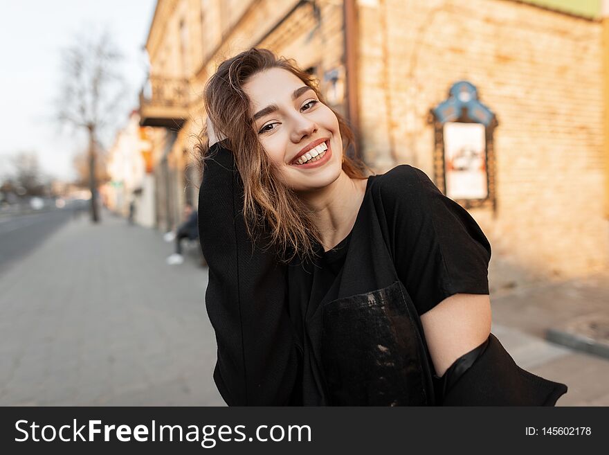 Young joyful beautiful woman with a wonderful smile in a stylish T-shirt in a elegant coat posing on a sunny day in the city