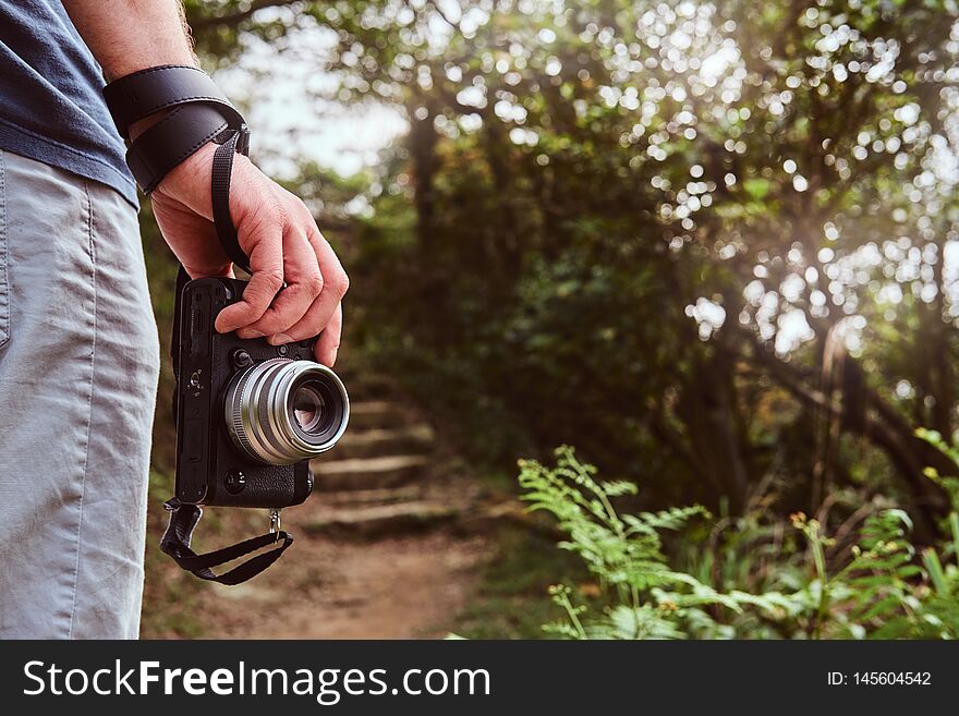 Man is holding camera in his hand while walking by the path throw the green mountains
