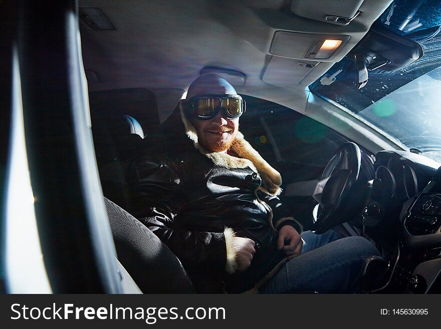 Funny male driver in a leather jacket in the car in the dark. Drunk driver in the car. Night unusual photo shoot. Funny male driver in a leather jacket in the car in the dark. Drunk driver in the car. Night unusual photo shoot