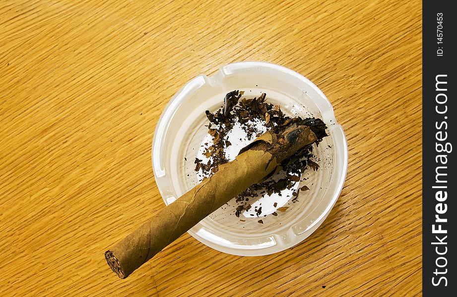 The broken extinct cigar lying in a white ashtray. The broken extinct cigar lying in a white ashtray