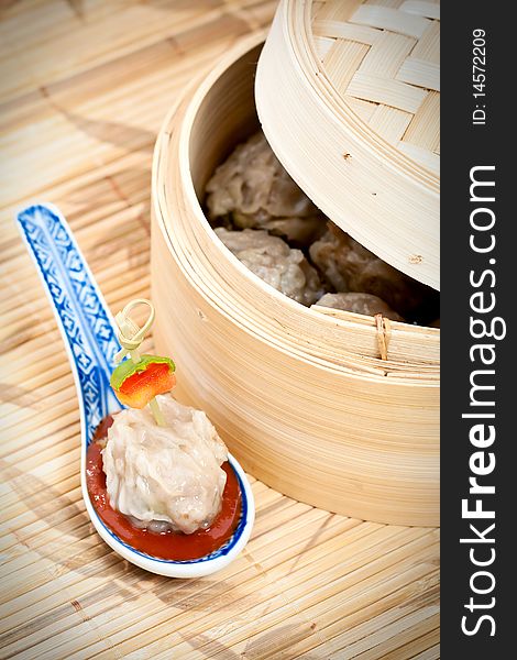 Traditional Chinese meal of dim sum or steamed dumplings on decorative spoon with harissa sauce and bamboo steamer.