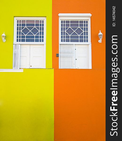 Two houses' white entrance doors, with one half of the walls brigh yellow, and the other half bright orange. Two houses' white entrance doors, with one half of the walls brigh yellow, and the other half bright orange