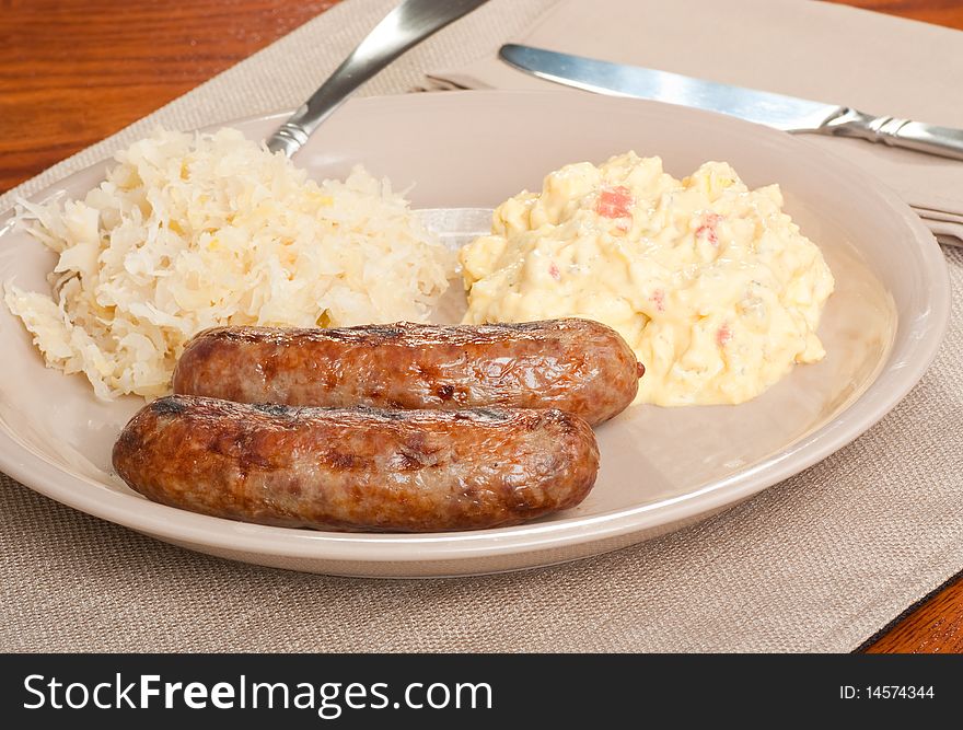 Two bratwursts on a plate with potato salad and sauerkraut