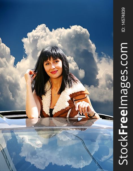 Beautiful brunette in the automobile on a background of the sky with clouds