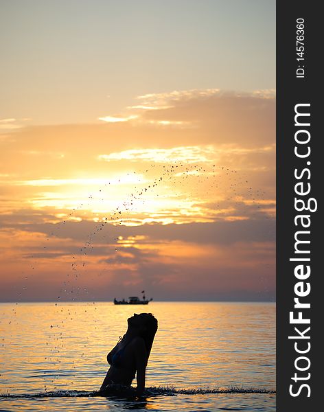 The girl sharply lifts wet hair from water. Decline. Silhouette. The girl sharply lifts wet hair from water. Decline. Silhouette.