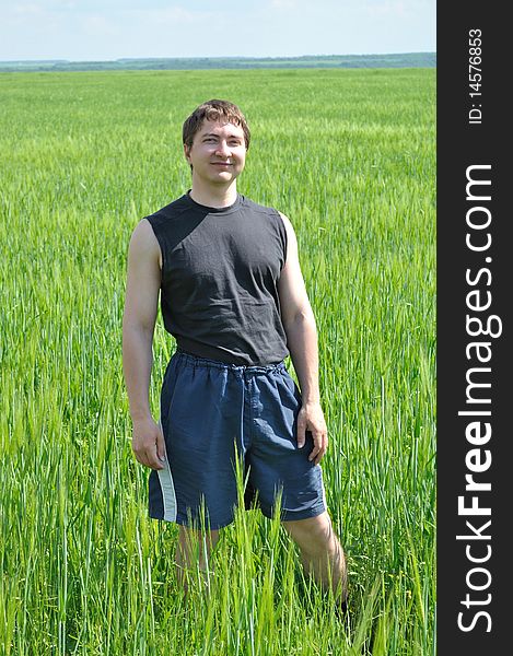 One man, standing in a field of green wheat, smiles. One man, standing in a field of green wheat, smiles