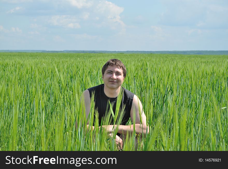 A Man Sits In A Field Of Green Wheat