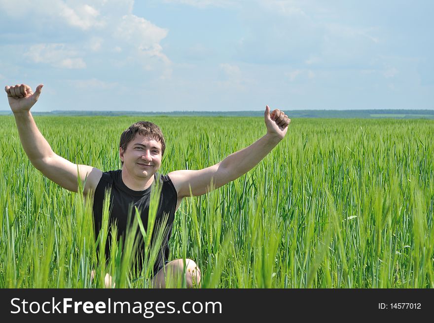 One man, sitting in a field of green wheat, smiles,raised his hands up. One man, sitting in a field of green wheat, smiles,raised his hands up