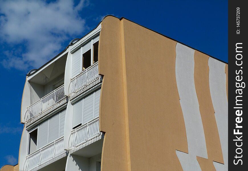 Part exterior elevation of concrete panel condominium building with blue sky above. trademark of multi unit residential architecture in Paks, Hungary. called the tulip building style. white balconies with roll down sun blind shades. Part exterior elevation of concrete panel condominium building with blue sky above. trademark of multi unit residential architecture in Paks, Hungary. called the tulip building style. white balconies with roll down sun blind shades.