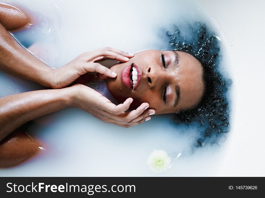 Young brown skin girl taking bath and lying in foam, wearing swimsuit. Concept of relax and