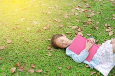 Little Girl Resting With Book Lying On Green Grass With Dried Leaves In The Summer Garden Stock Image