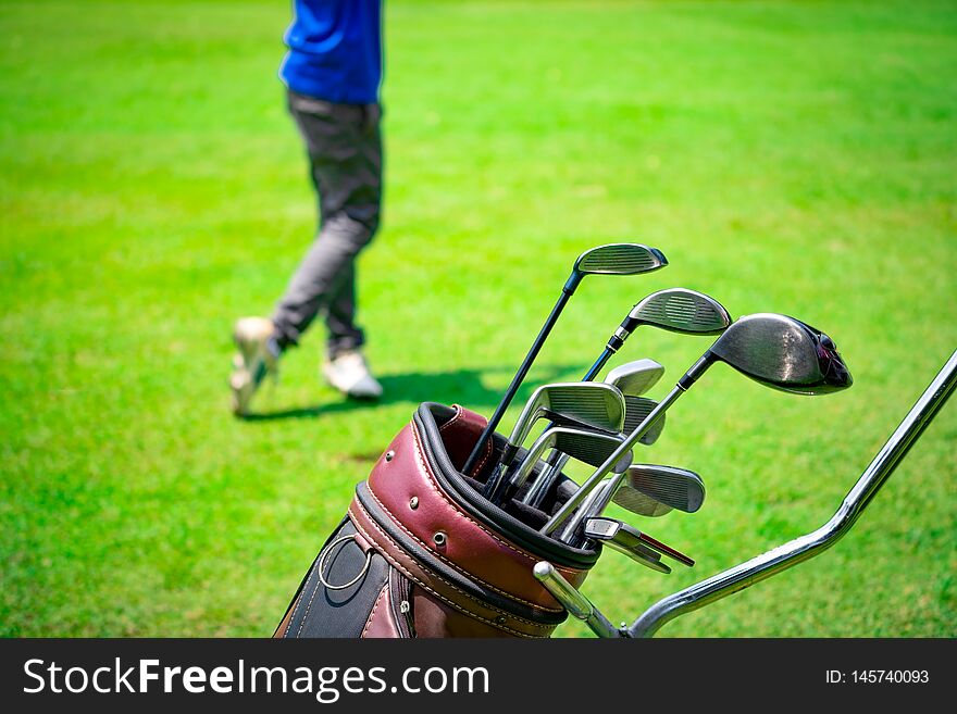 Golf club suit in bag cart and blurred golfer hitting golf ball on green golf course on summer time