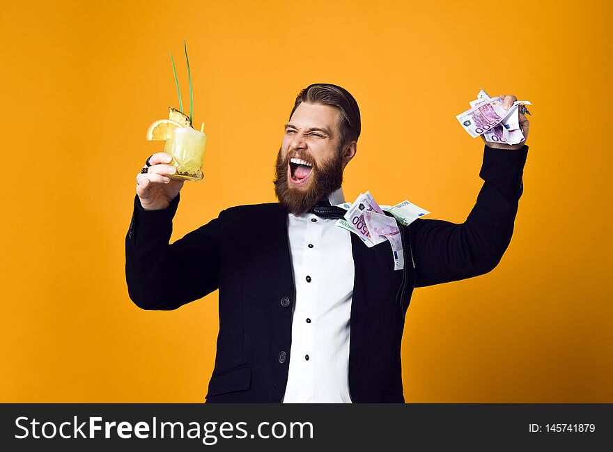 I am rich! Happy young businessman with glass of cocktail in formal clothes holding bunch of money banknotes and celebrating throwing money up