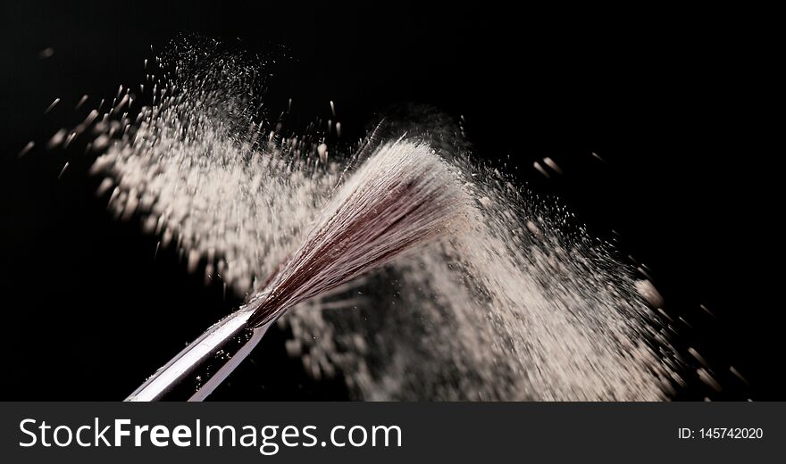 Fine art cosmetic, makeup concept with a highlighted soft bristle brush and a puff of facial powder on a black background with