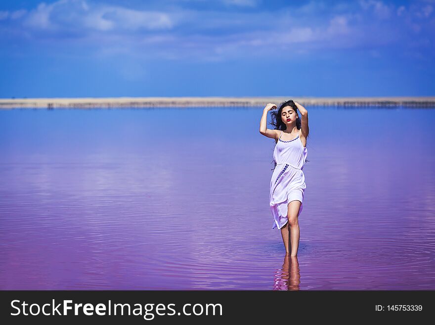 Beautiful young girl in long white dress posing on salty pink lake.
