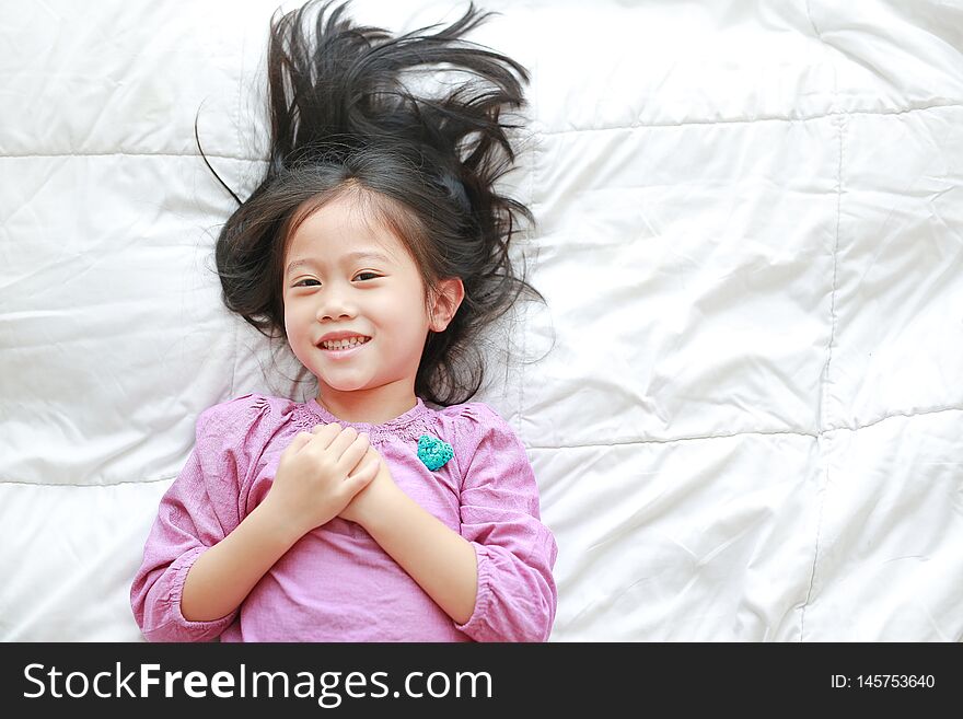Smiling little Asian child girl lying on bed looking at camera. Above view