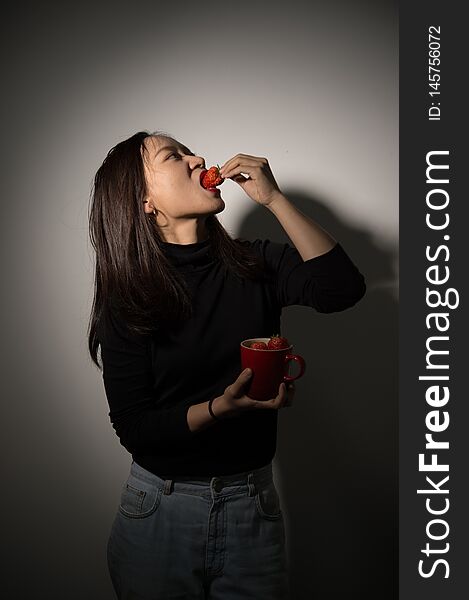 Studio shot of a beautiful asian girl eating fresh strawberries. Studio shot of a beautiful asian girl eating fresh strawberries