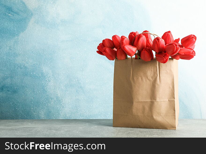 Paper bag with beautiful red tulips on table against blue background