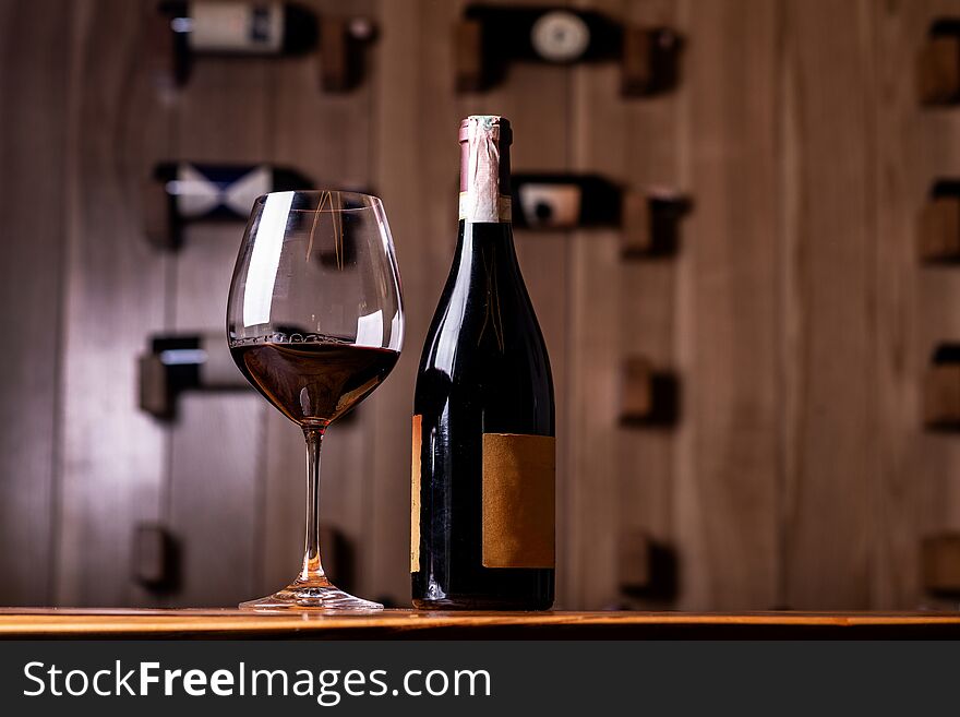 Glass and bottle with delicious red wine on wooden table. In the background Red wine bottles stacked on wooden racks shot with limited depth of field