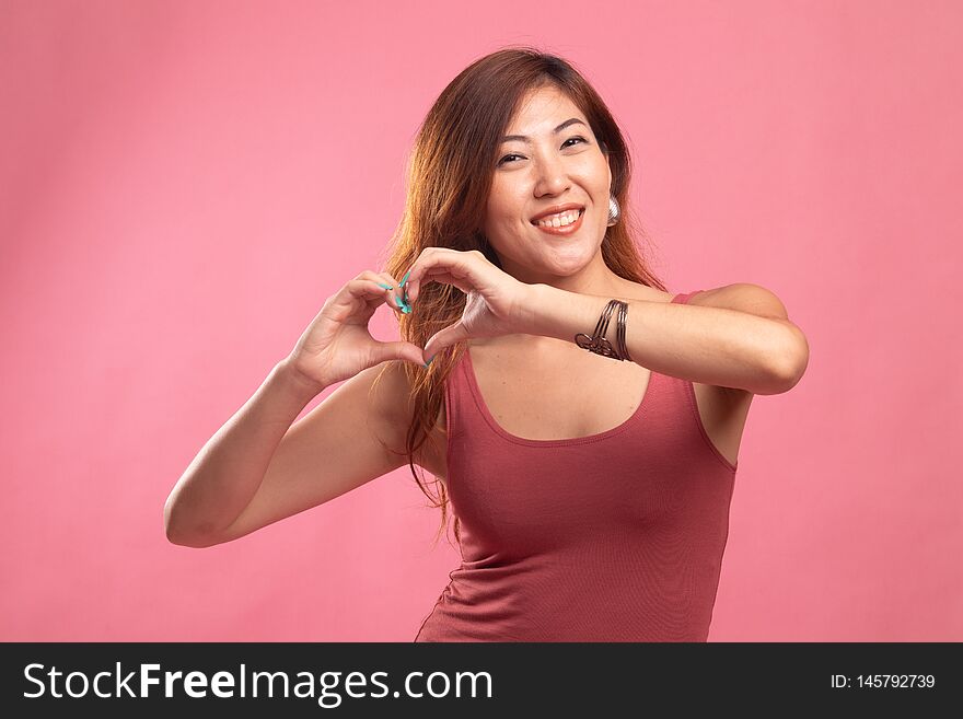 Young Asian woman show heart hand sign on pink background