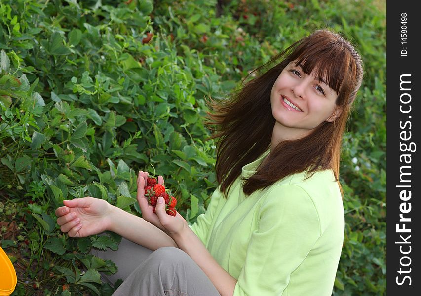 A smiling woman picking strawberries in a field closeup