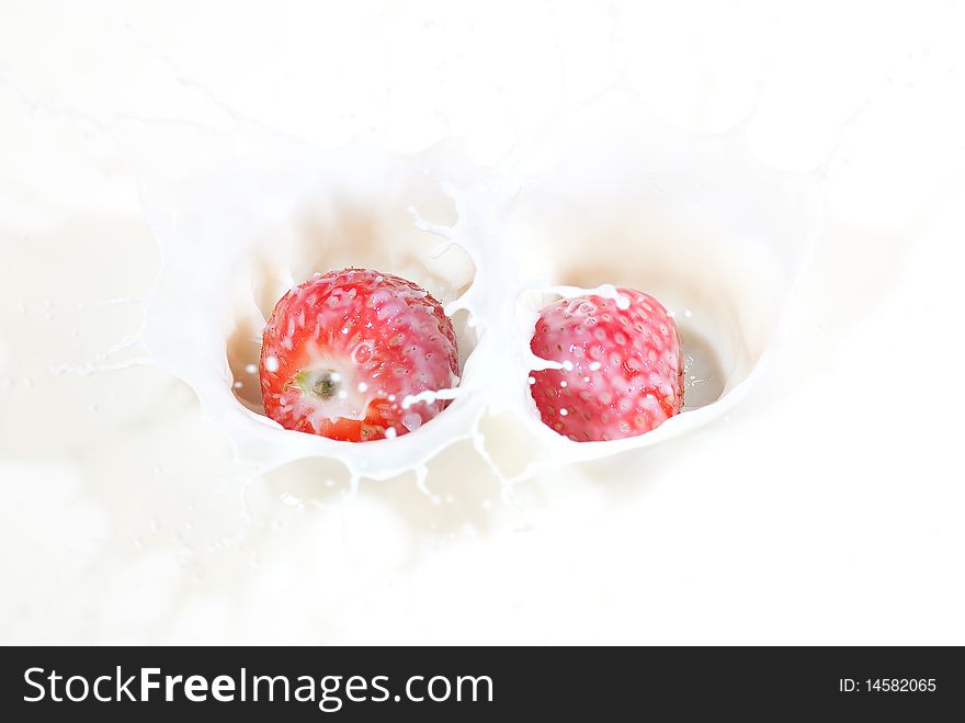 A Couple Of Fresh Strawberries Splashing Into Milk