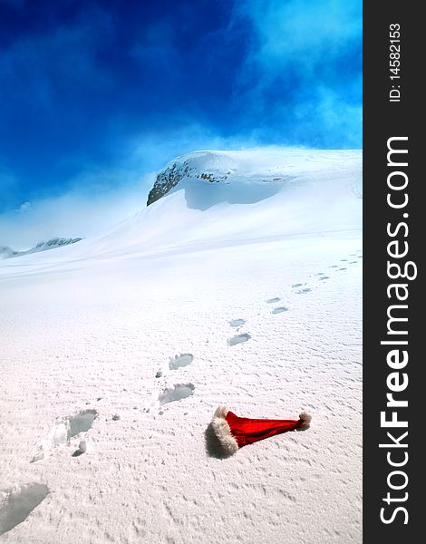 Santa's hat lying on a snow on a backgrounds of a mountains and blue sky. Santa's hat lying on a snow on a backgrounds of a mountains and blue sky