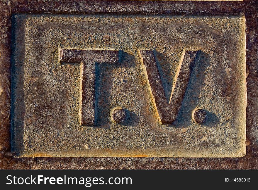 A metallic sign which is rusty and brown spelling TV. A metallic sign which is rusty and brown spelling TV
