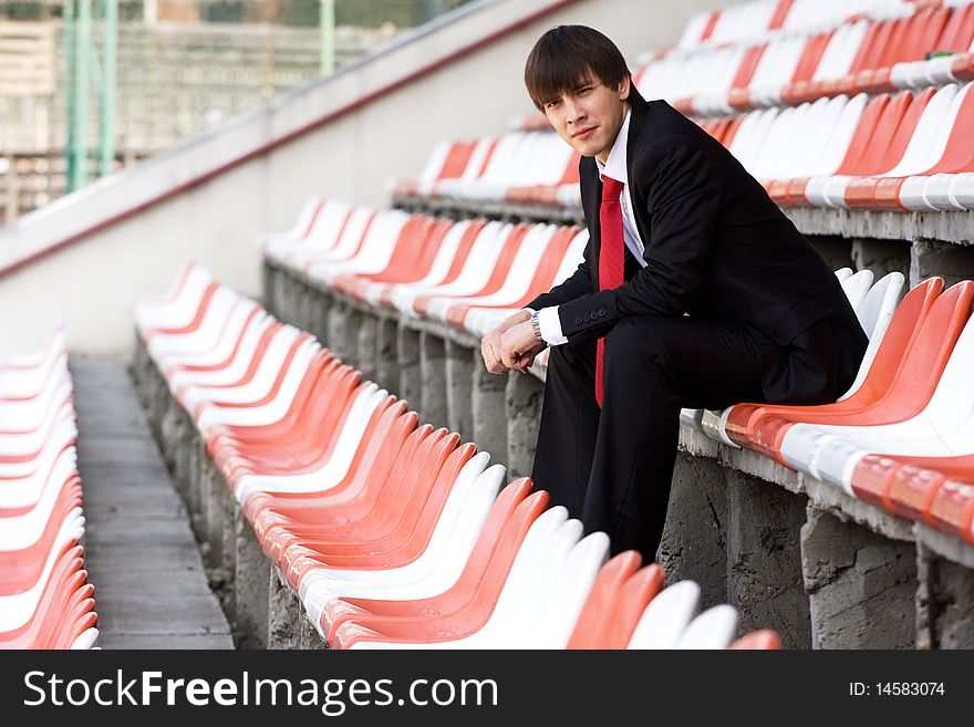 Young man in black suit sitting on the audience bleachers. Young man in black suit sitting on the audience bleachers