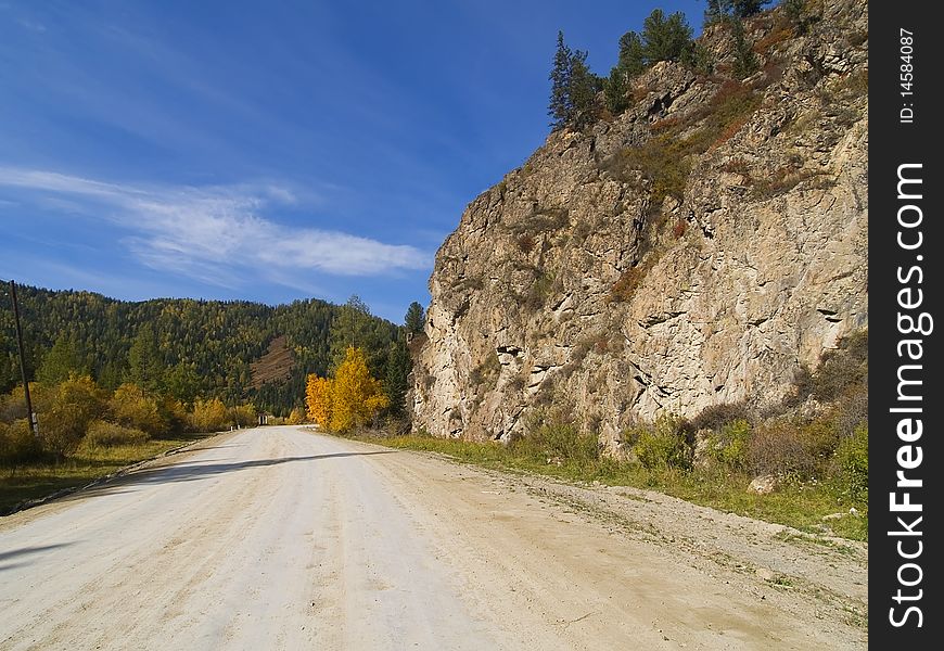 Dirt road in the mountains with forests, rocks and sky with clouds