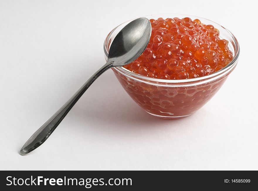 Red caviar in the little glass bow and spoon isolated over grey gradient background