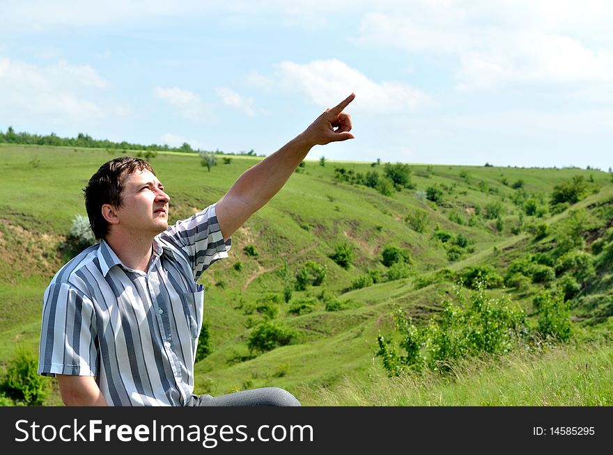 A young man sits and shows the direction of finger. A young man sits and shows the direction of finger