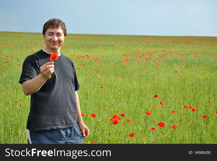 A young man holds a poppy flower, against a background of poppy field