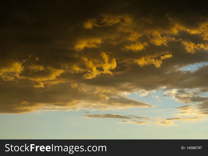 Dramatic storm clouds, colored partly orange due to the setting sun, with blue skies behind