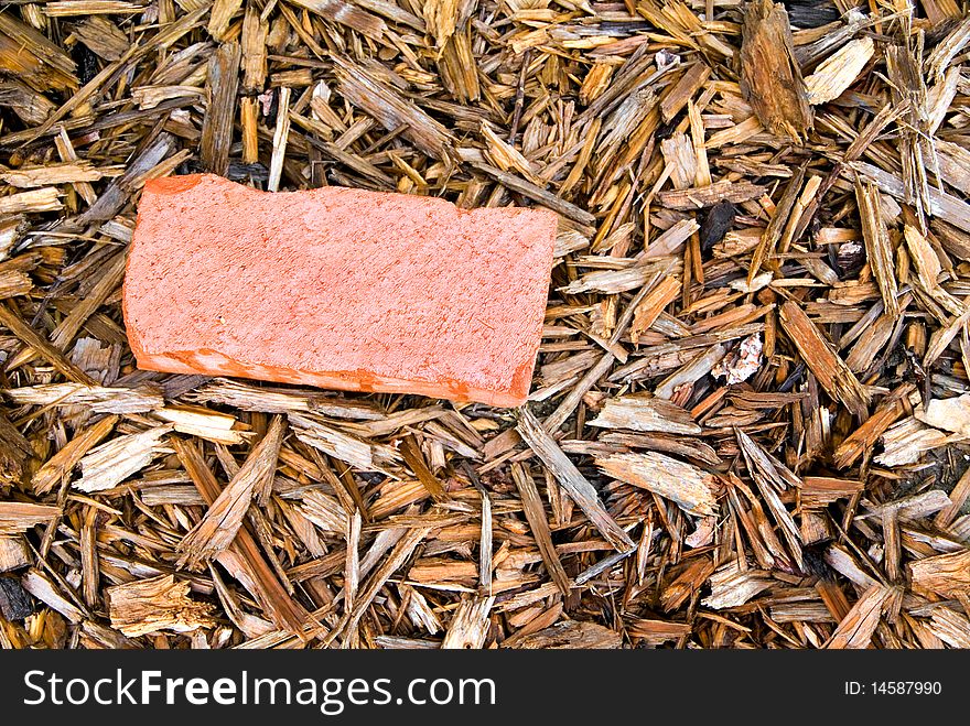 A red brick laying in a bed of wood mulch. A red brick laying in a bed of wood mulch.