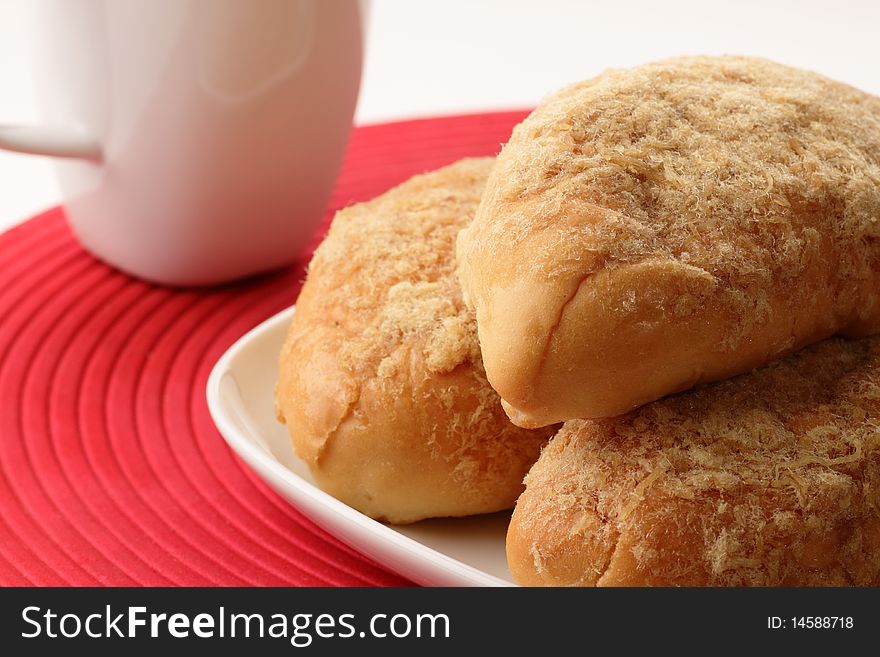 A plate of chicken floss buns and a cup of coffee on a red place mat with white background