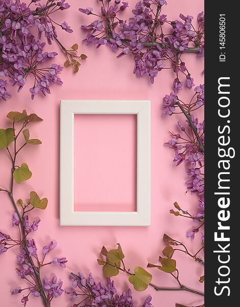 Flowers composition. Purple flowers, leaves and photo frame on pastel pink background
