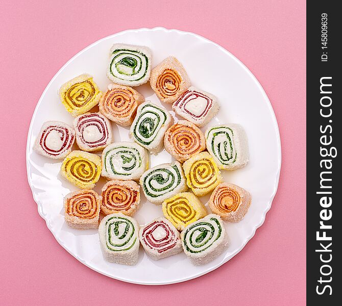 Turkish sweets of different colors on a white plate on pink background