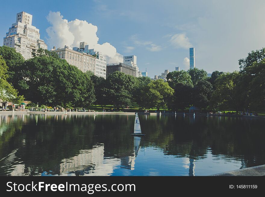 A Reflecting Lake In A Park With Tall Buildings And Beautiful Sky