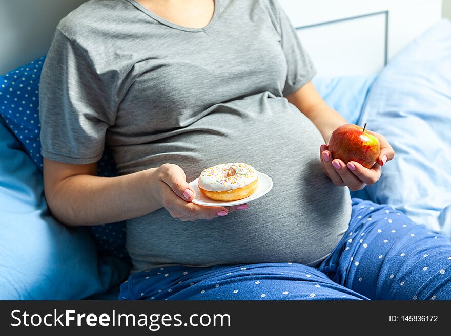 Pregnant Woman With Stomach And Holding An Apple And Donut. Diet For Pregnant Women.