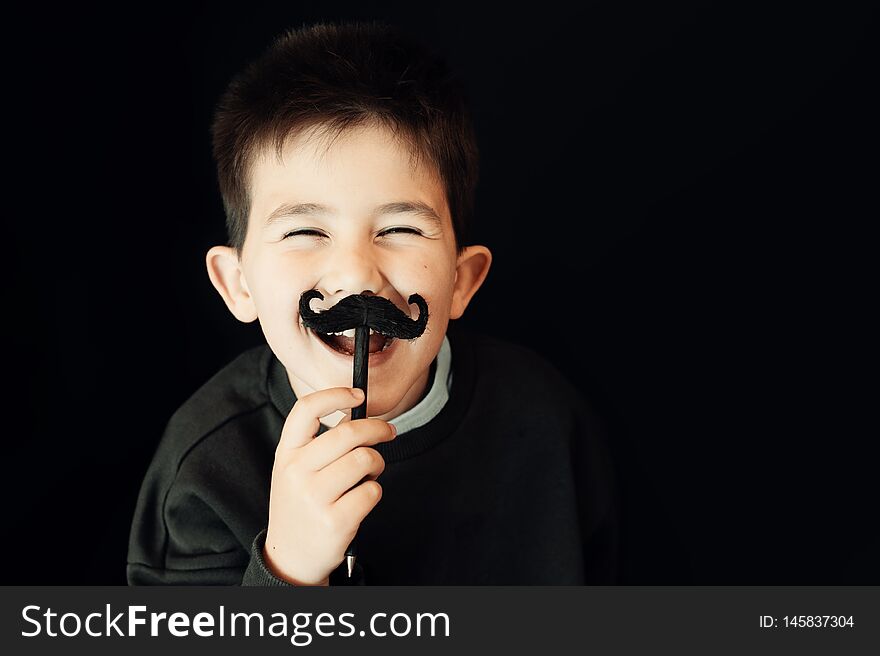 Happy kid posing with a fake moustache on black background.