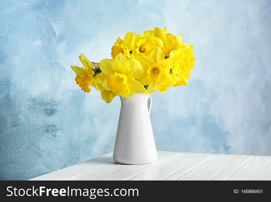 Bouquet of daffodils in jug on table against color background. Fresh spring flowers